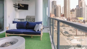Un balcon avec un canapé bleu, un petit barbecue et un téléviseur.