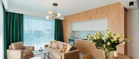 Una sala moderna con sofá, mesa de centro y mesa de comedor. Cuenta con una cocina con armarios de madera y vistas a la ciudad.