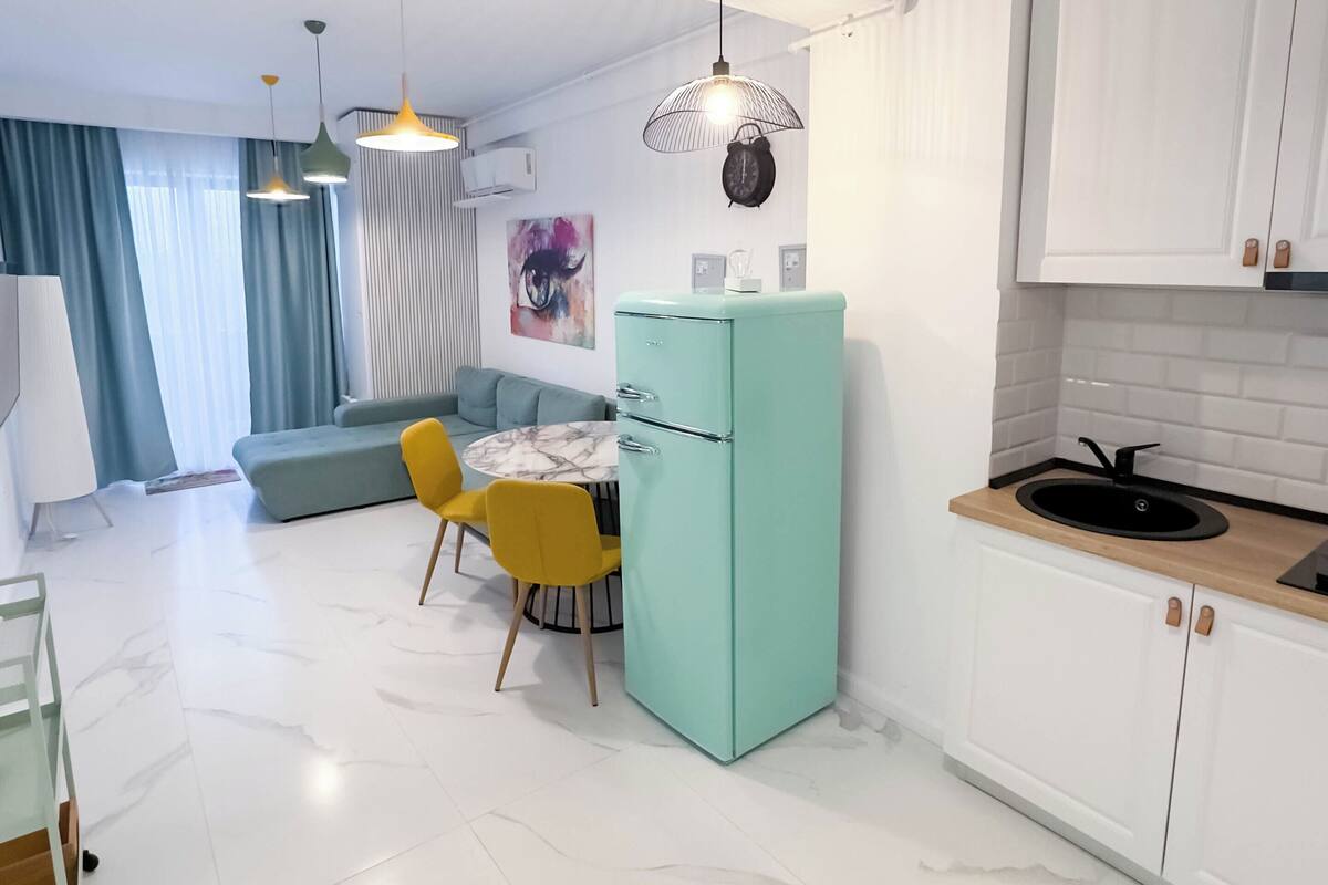 Una cocina moderna con armarios blancos, un refrigerador verde azulado y un lavamanos negro.