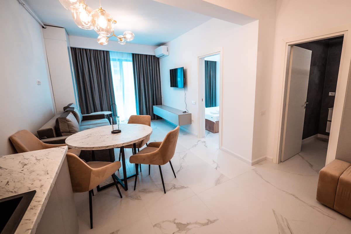 Una sala de estar moderna con suelo de mármol, una mesa redonda de comedor con sillas, un sofá y un televisor montado en la pared.