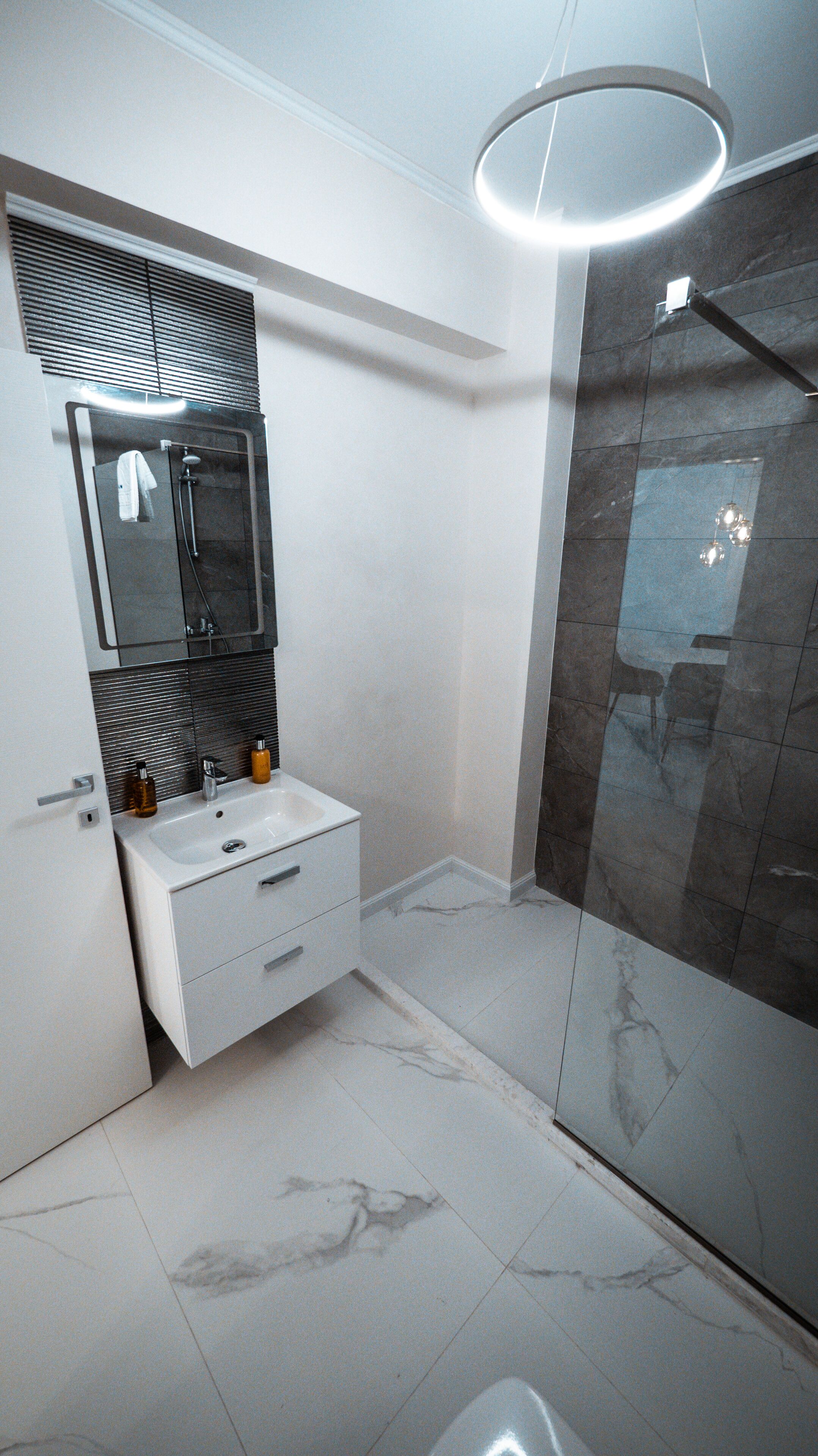 Une salle de bain moderne avec une douche à parois de verre, un meuble-lavabo blanc doté d’un miroir et un luminaire fixé au plafond.