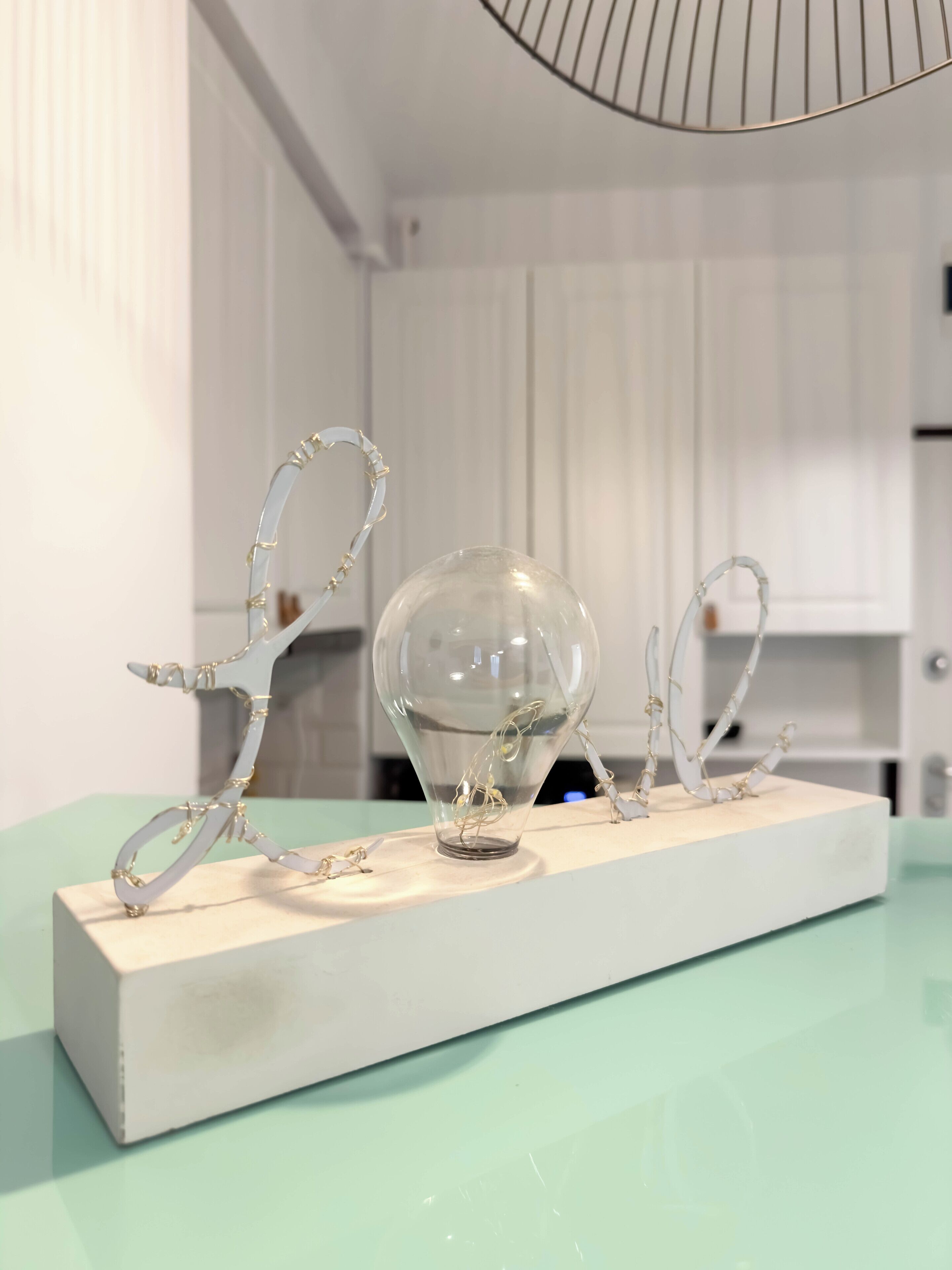 Esposizione di vetreria e sculture in metallo su una piattaforma bianca, in una stanza con pareti bianche e pavimento verde chiaro.
