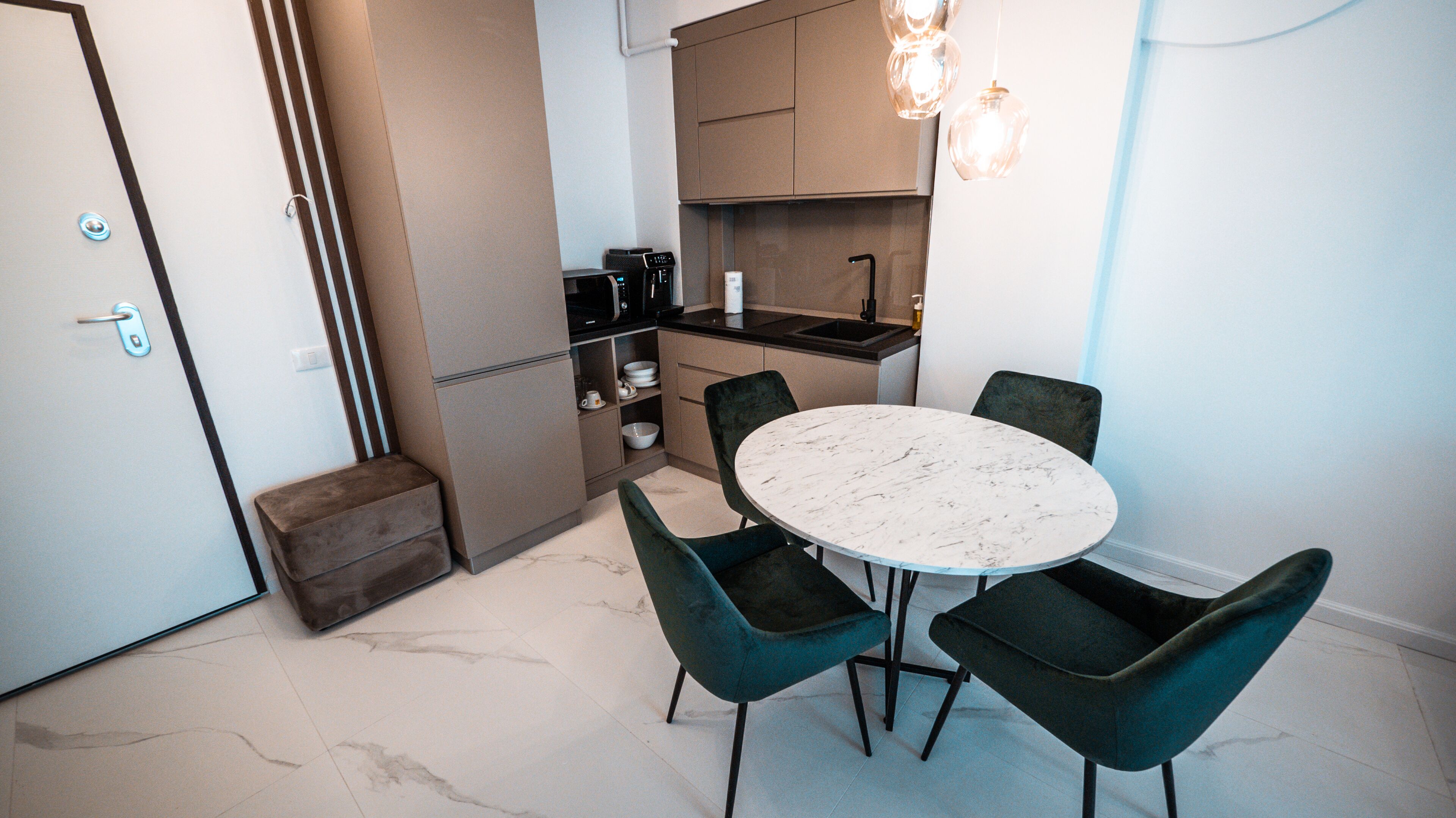 A compact kitchen with a dining area, including a marble table and dark chairs.