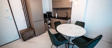 A compact kitchen with a dining area, including a marble table and dark chairs.