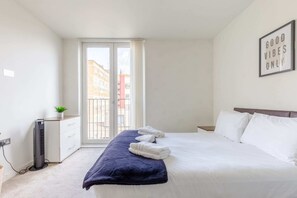 A hotel room with a bed, a bedside table, a heater, a window with a view of buildings, and a wall with a sign saying "GOOD VIBES ONLY". - Radiant 1BD Retreat, North Maida Vale! (London)