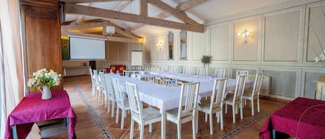 A conference room with a long table, white chairs, and a projector screen.