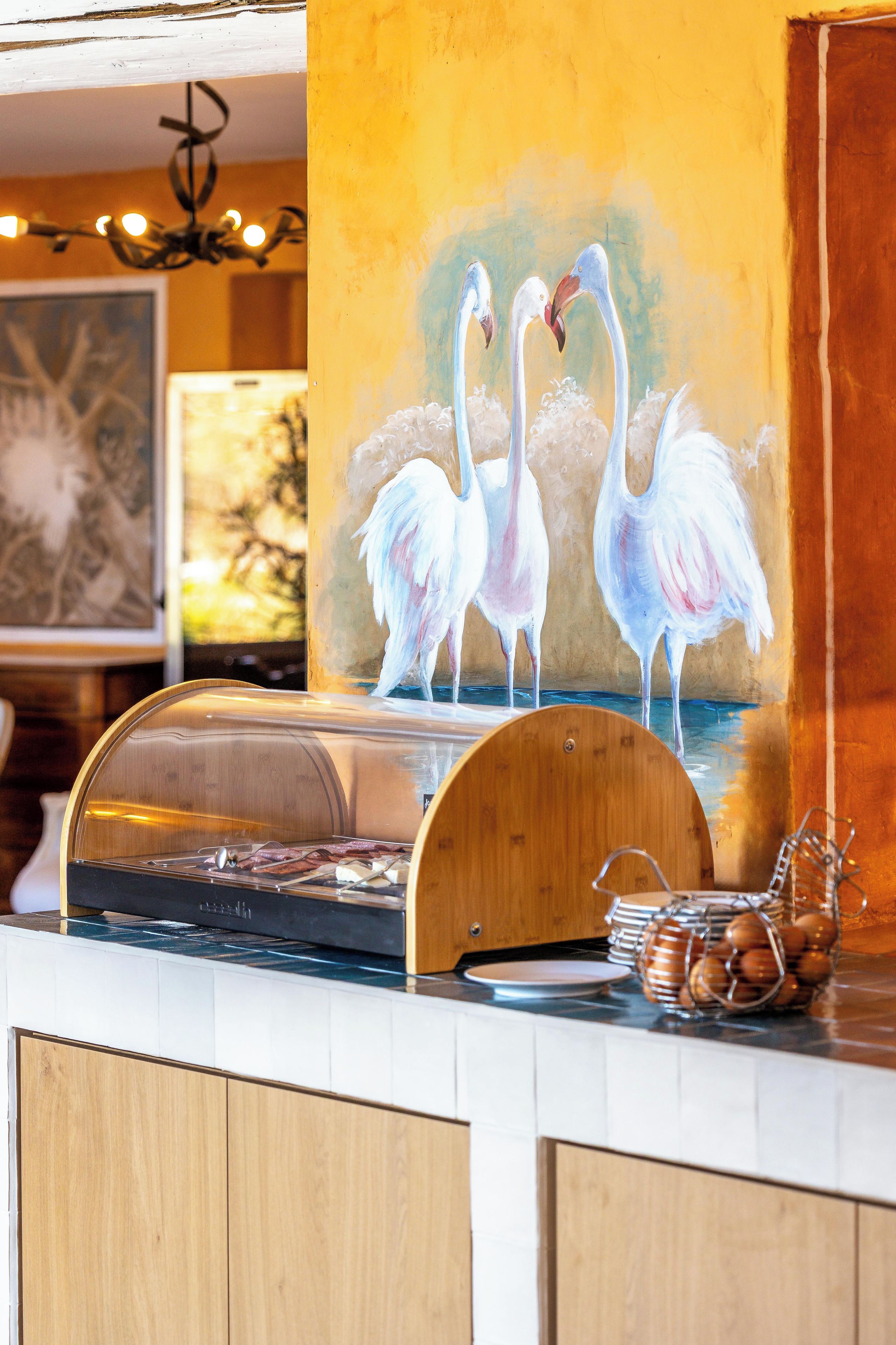 Un espace buffet doté d’un comptoir en bois, d’une vitrine et d’un tableau représentant des flamants roses.