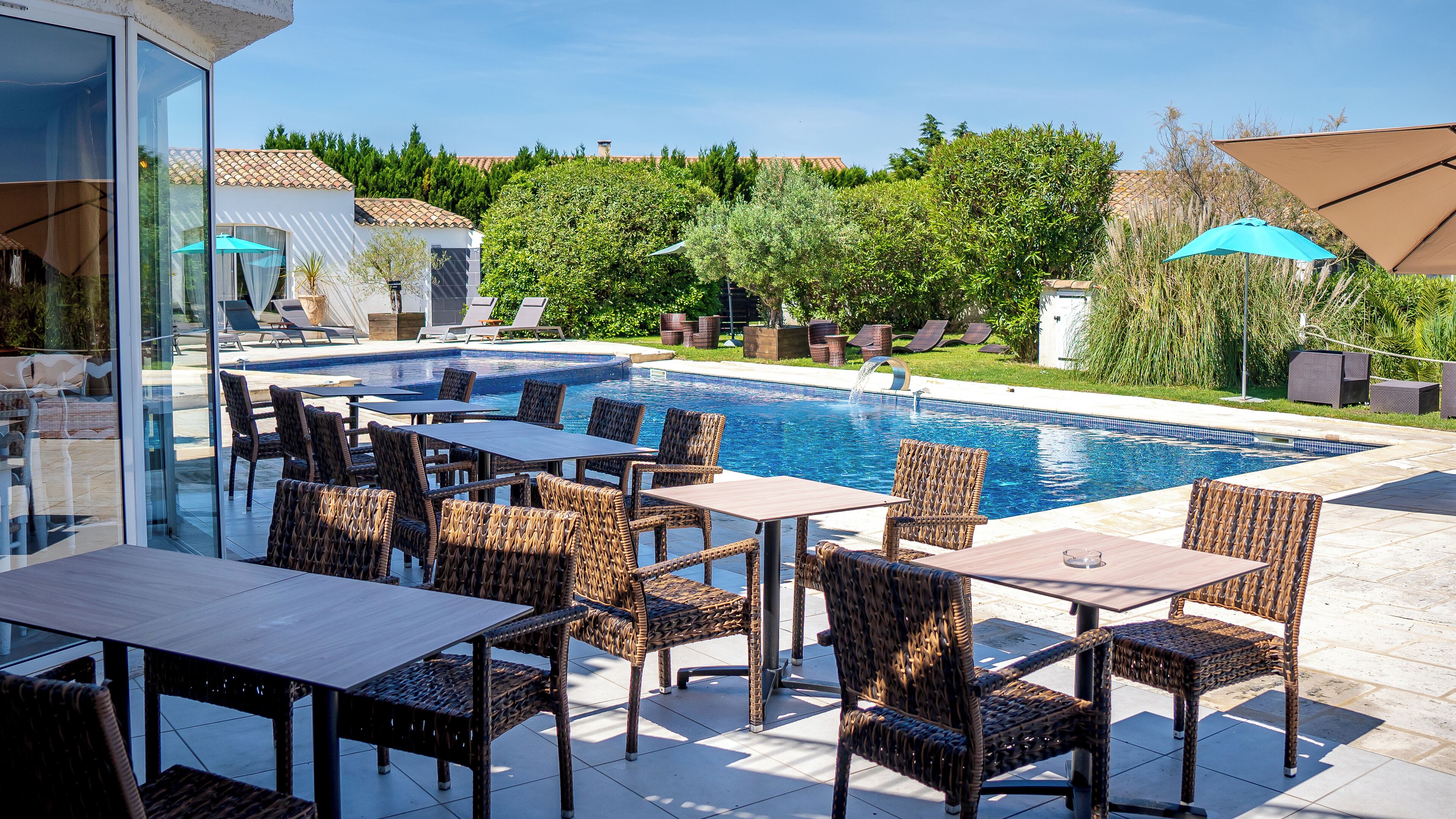 An outdoor pool area with wicker furniture, a clear blue pool, and a view of the surrounding greenery.