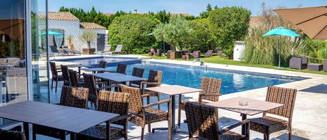 An outdoor pool area with wicker furniture, a clear blue pool, and a view of the surrounding greenery.