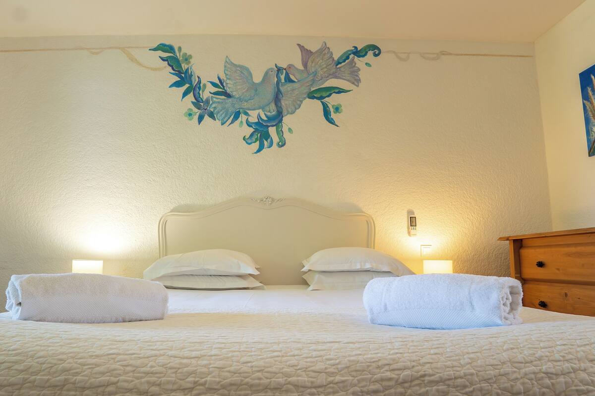 Une chambre à coucher avec un lit, deux lampes de chevet, une commode en bois et une fresque murale.