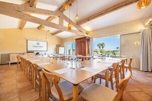 A conference room with a long table, chairs, a projector screen, and a view of the outdoors.