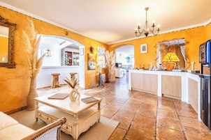 Una cocina amplia con una isla central, un comedor con mesa y sillas, y una sala de estar con sofá y objetos decorativos.