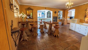 Un interior rústico con mesas y taburetes de madera, una araña y vistas al exterior.