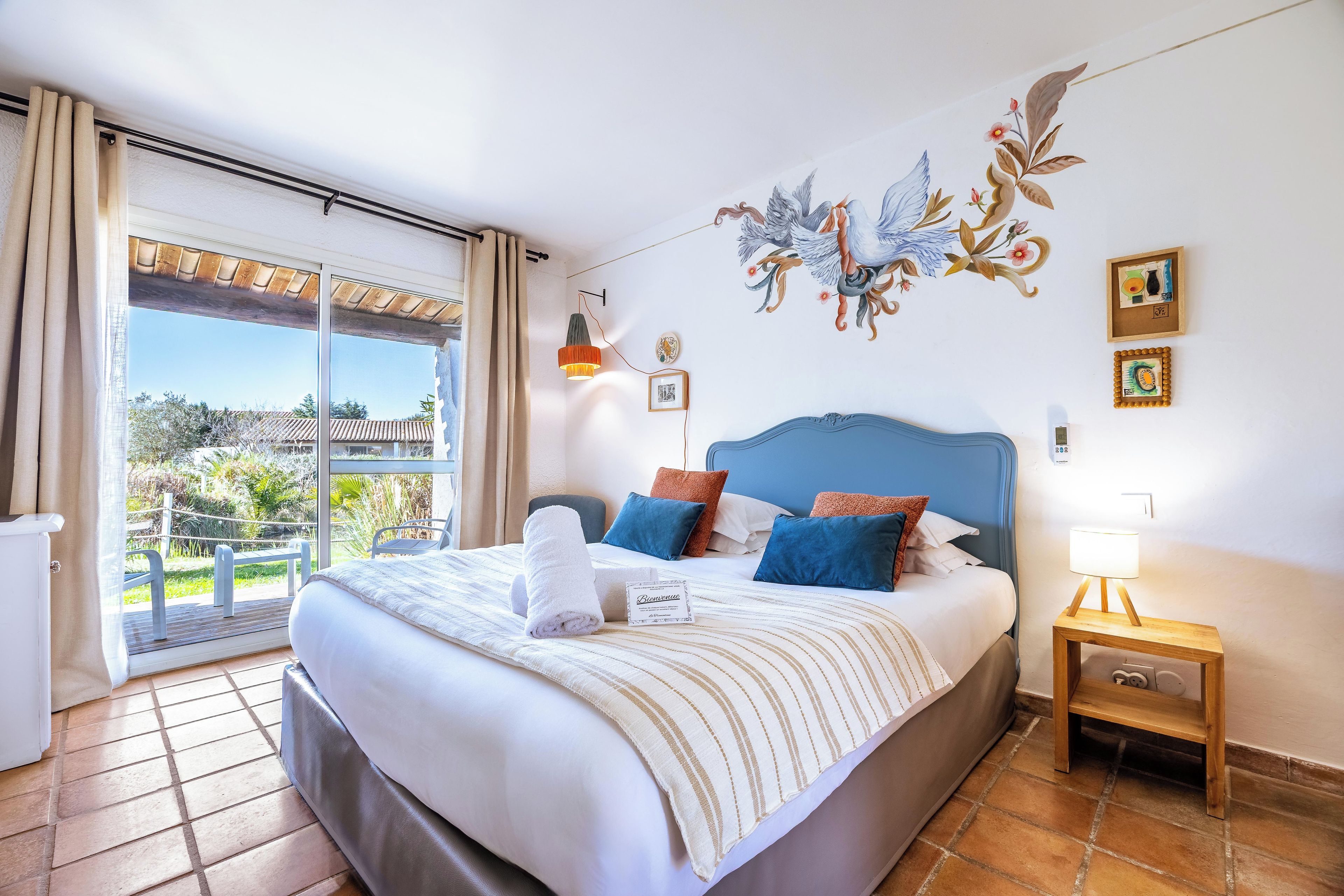 Ein Hotelzimmer mit Bett, Nachttisch, Lampe und Blick ins Freie.