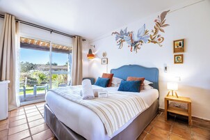 A hotel room with a bed, a bedside table, a lamp, and a view of the outdoors.