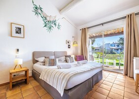 Un dormitorio con cama, mesita de noche, lámpara y vistas al exterior.