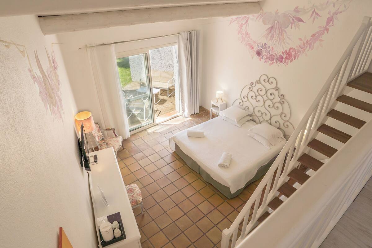 Une chambre à coucher comprenant un lit, une table de chevet, une lampe, une chaise et donnant sur le balcon extérieur.