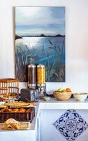 Um buffet de café da manhã com diversos alimentos, uma pintura de uma paisagem e um piso de azulejos.
