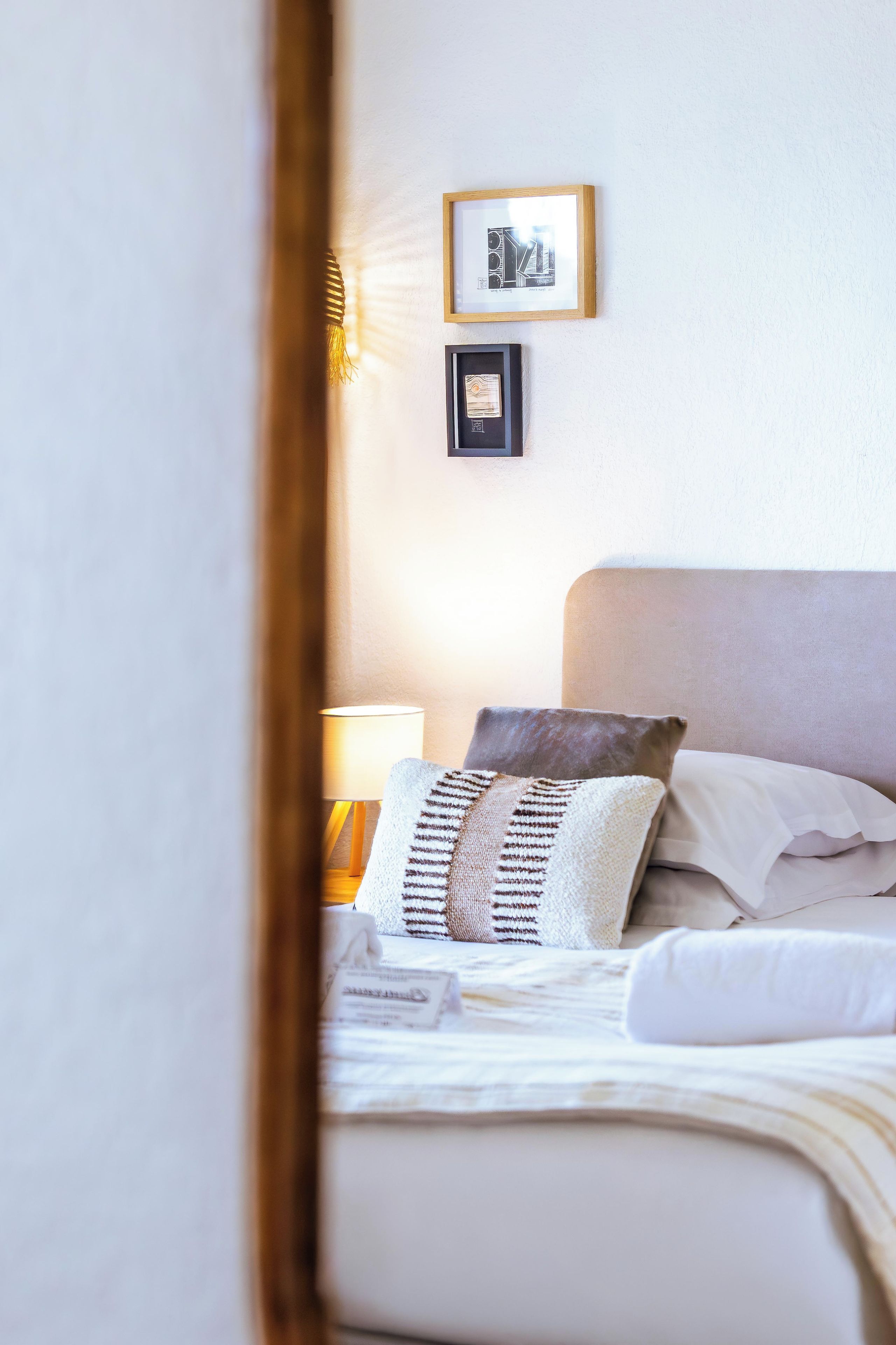 Un lit bien fait, avec des oreillers et une couverture, une lampe de chevet et deux tableaux encadrés accrochés au mur.
