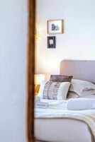 Una cama bien hecha con almohadas y una manta, una lámpara de noche y dos cuadros en la pared.