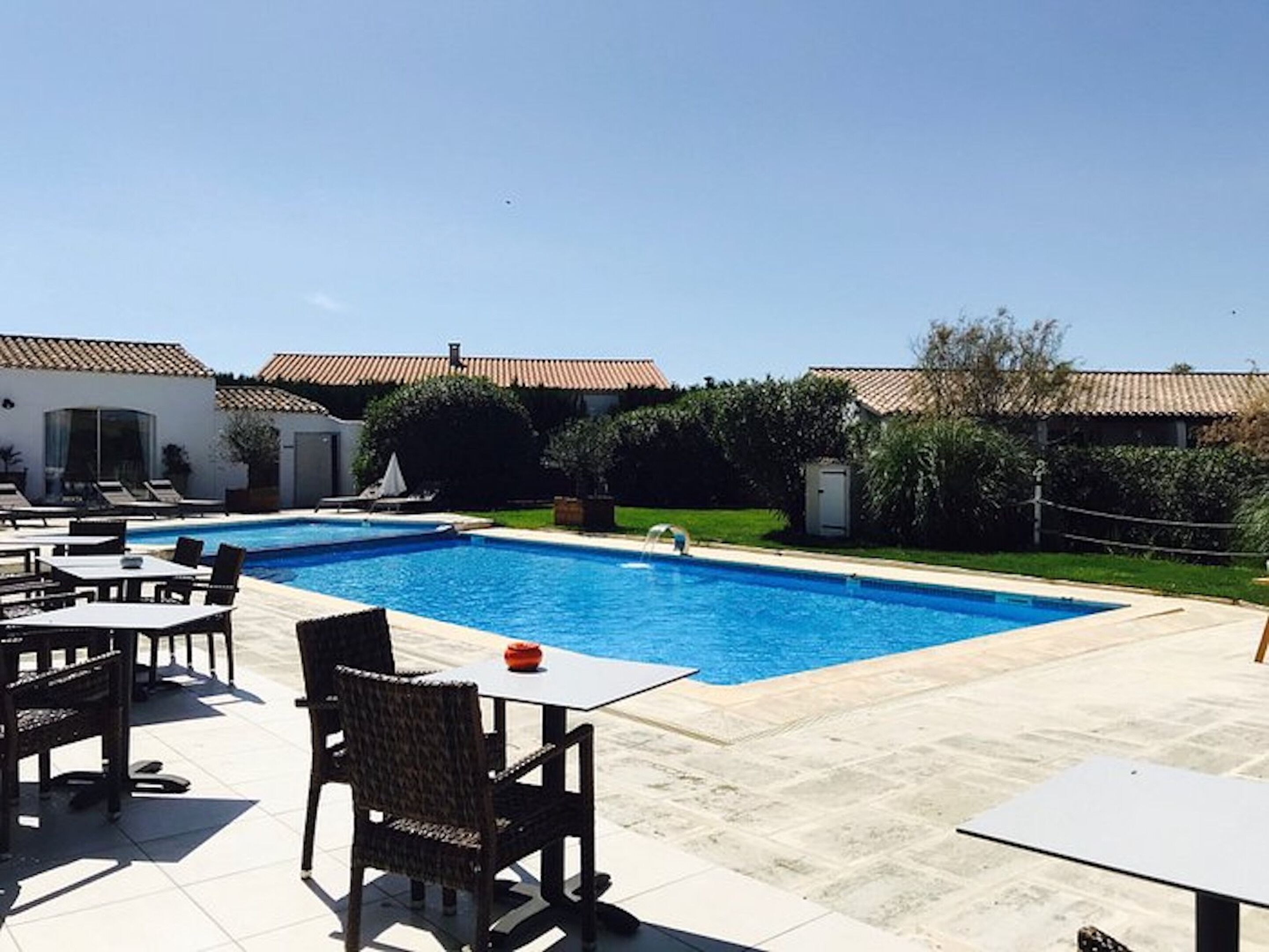 Una piscina con lettini e tavoli, circondata da edifici con tetti in tegole.