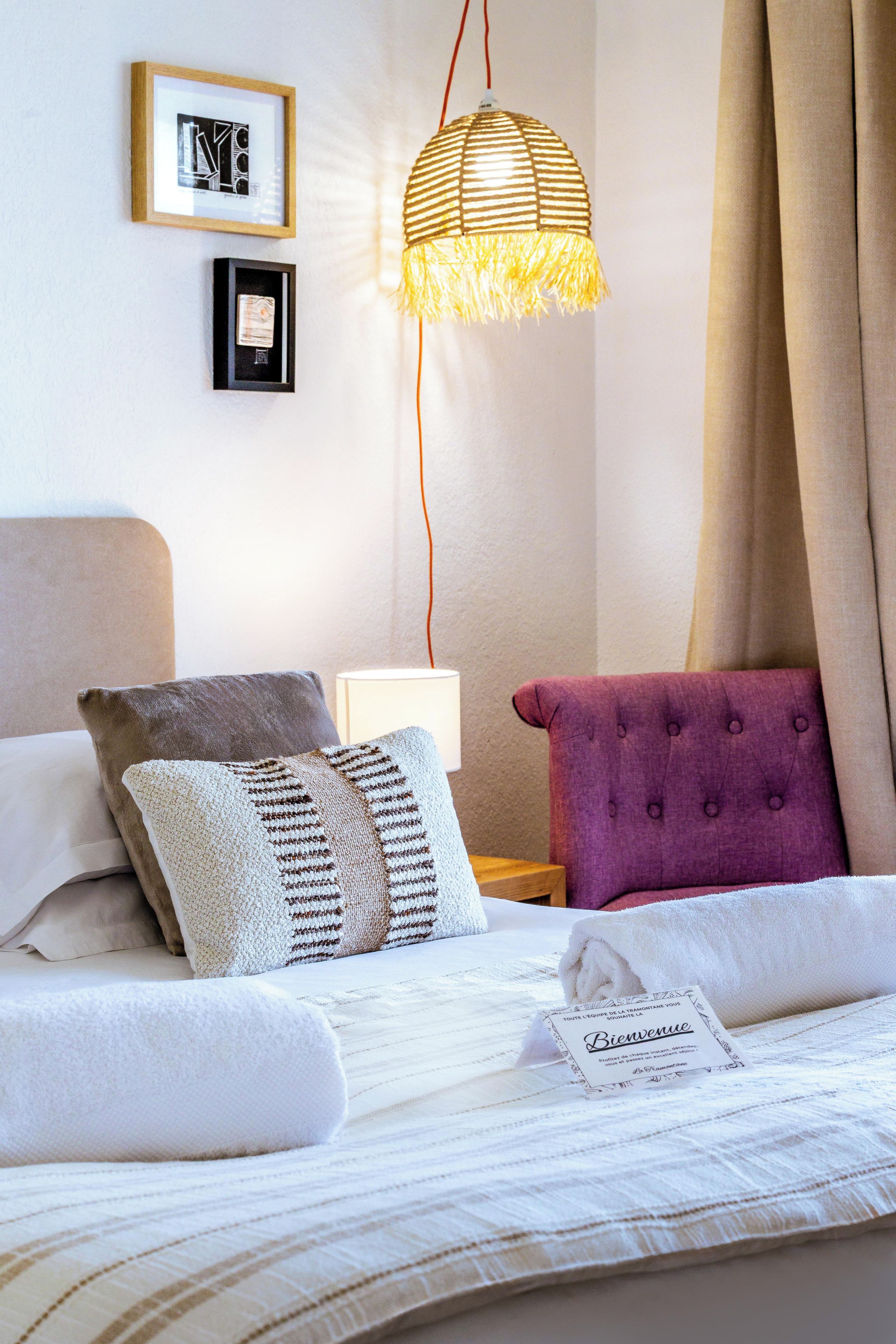 A neatly made bed with a white comforter, a rolled towel, and a welcome card.