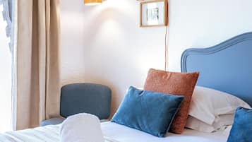 Una cama bien hecha con una toalla blanca, un cartel de bienvenida enmarcado y una lámpara fijada a la pared.