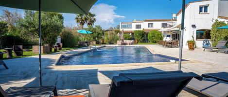 A swimming pool with lounge chairs and umbrellas, surrounded by a patio area with outdoor furniture.