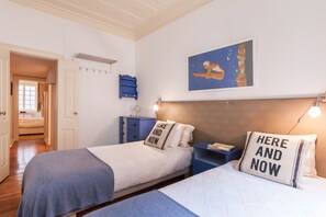 A bedroom with two beds, a blue nightstand, a white headboard, a wall-mounted shelf, and a door leading to another room. - 2 bedroom next to Avenida da Liberdade (Lisboa)