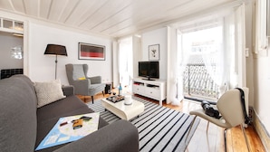 Ein modernes Wohnzimmer mit einem grauen Sofa, einem Couchtisch, einem Fernseher und einem Balkon mit Metallgeländer.