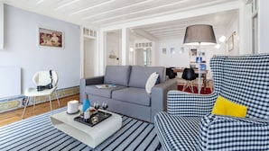 Ein modernes Wohnzimmer mit grauem Sofa, kariertem Sessel und einem weißen Couchtisch mit Kerze und Weingläsern.