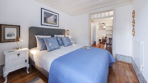 Ein Schlafzimmer mit einem großen Bett, einem Nachttisch, einem gerahmten Bild und einer Tür zu einem anderen Raum.