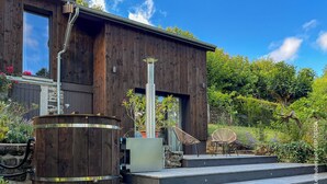 Un edificio moderno de madera con un amplio ventanal, una chimenea de metal y un barril de madera.