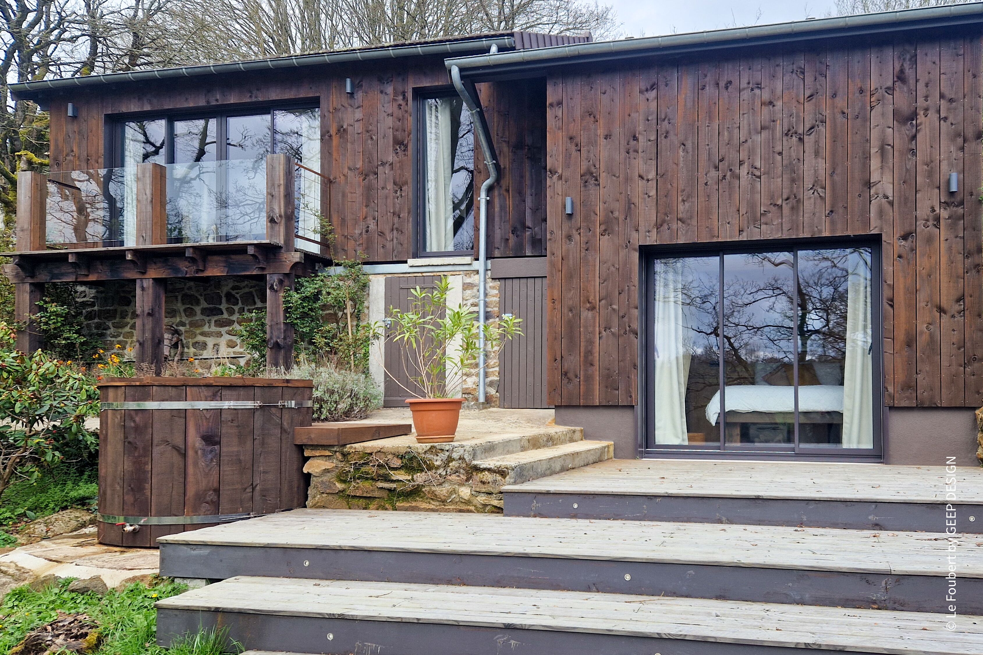 Ein modernes Holzhaus mit Steinunterbau, großen Fenstern und einer Holzterrasse.