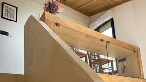 Una escalera moderna con escalones de madera y barandillas de vidrio, que conduce a una plataforma de madera con un jarrón de flores.