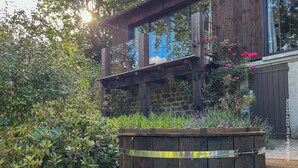 Una casa moderna de madera con base de piedra, ventanas amplias y un balcón con flores.