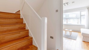 Un escalier en bois mène à une pièce dont le mur est blanc, qui possède une fenêtre et une petite table.