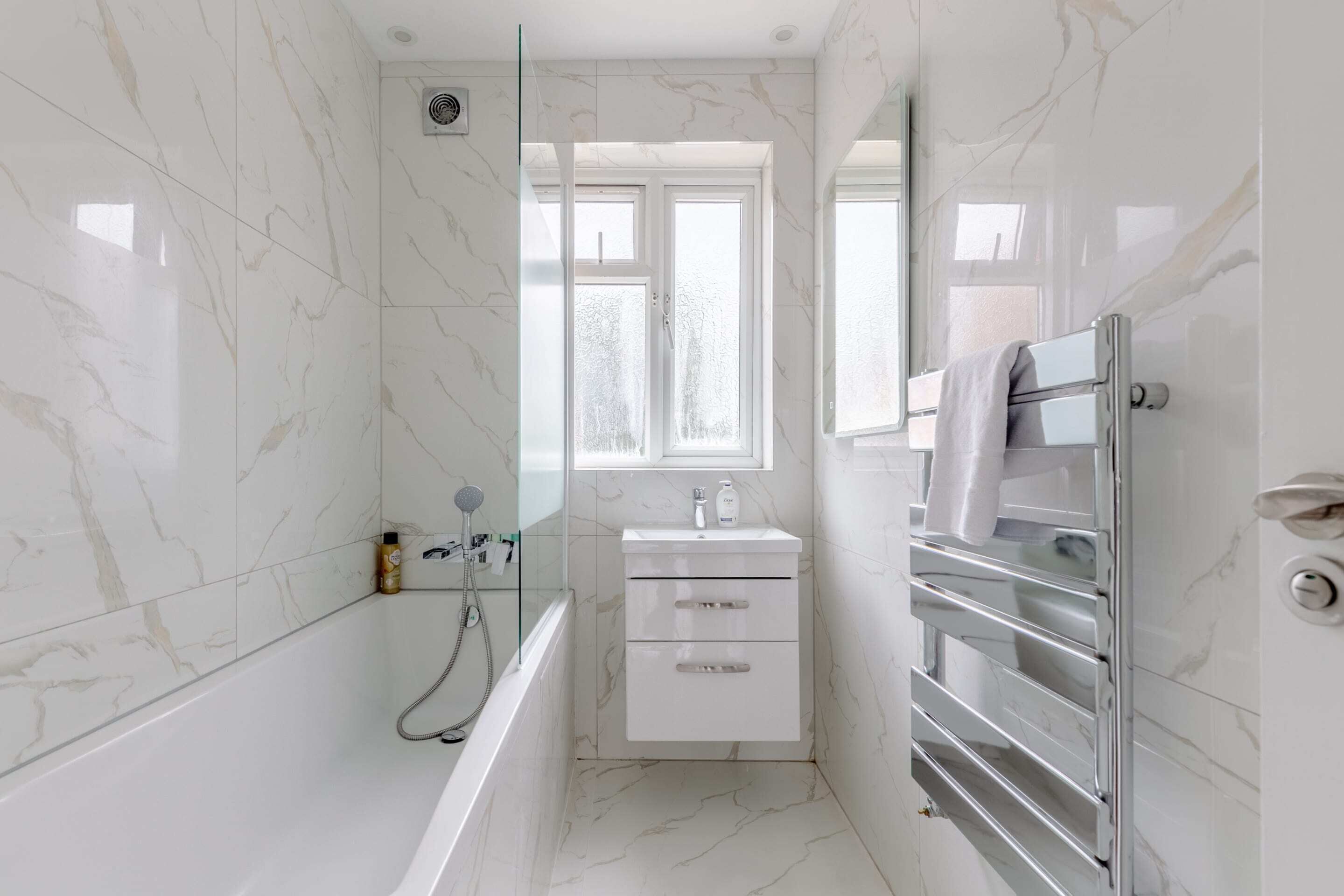 A modern bathroom with a glass-enclosed shower, a white sink, and a towel rack.