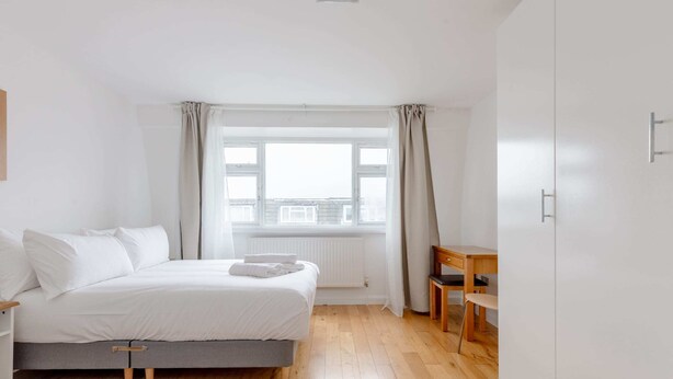 Une chambre avec deux lits, un plancher en bois, une fenêtre avec des rideaux, un radiateur et une chaise en bois.