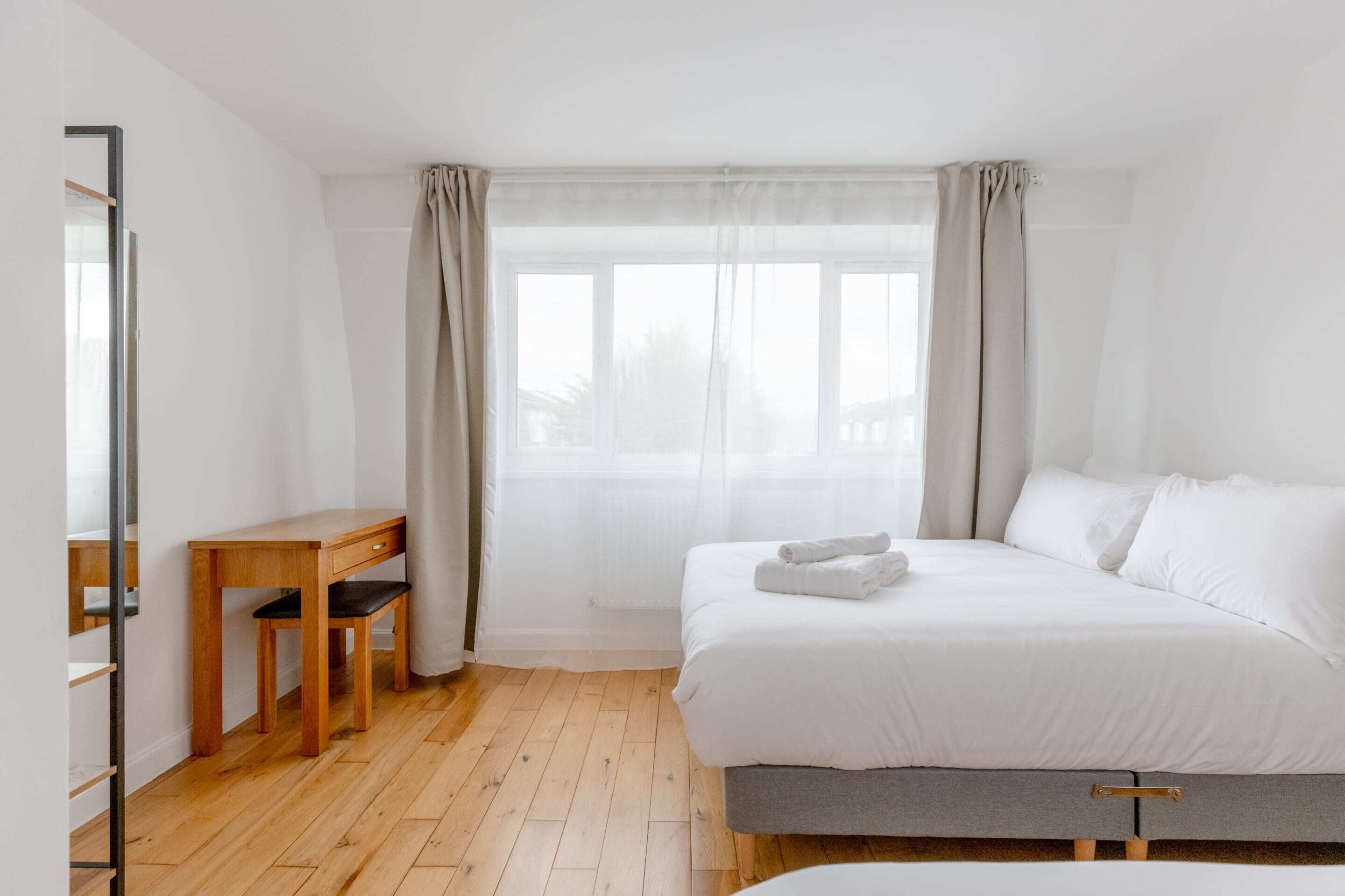 Een slaapkamer met een bed, een bureau en een raam met gordijnen.