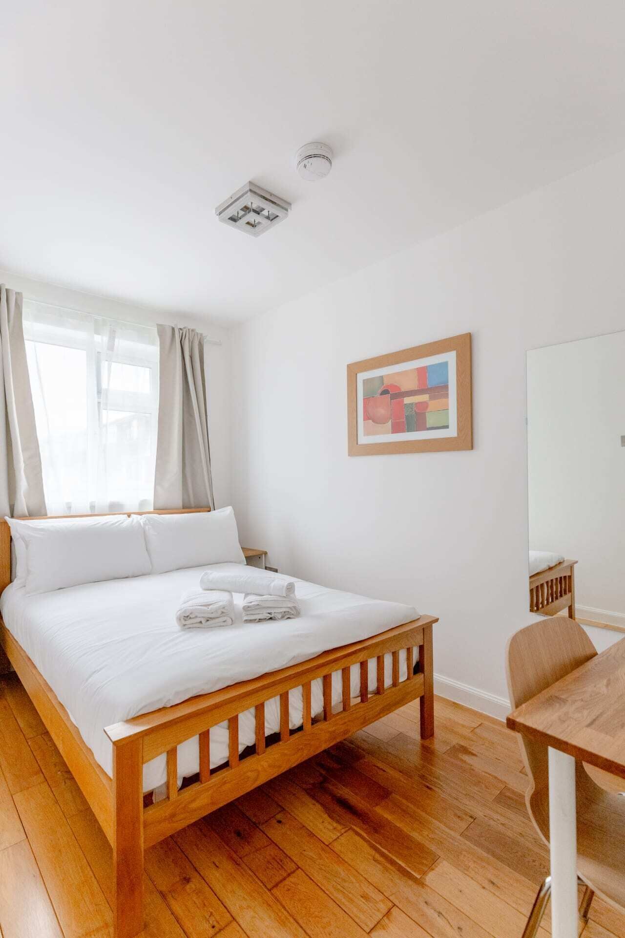 Un dormitorio con una cama de madera, ropa de cama blanca, una mesita pequeña y un cuadro en la pared.