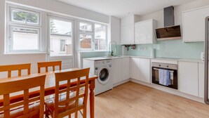 Une cuisine moderne avec des meubles blancs, un lave-linge encastré et un coin repas avec des chaises en bois.