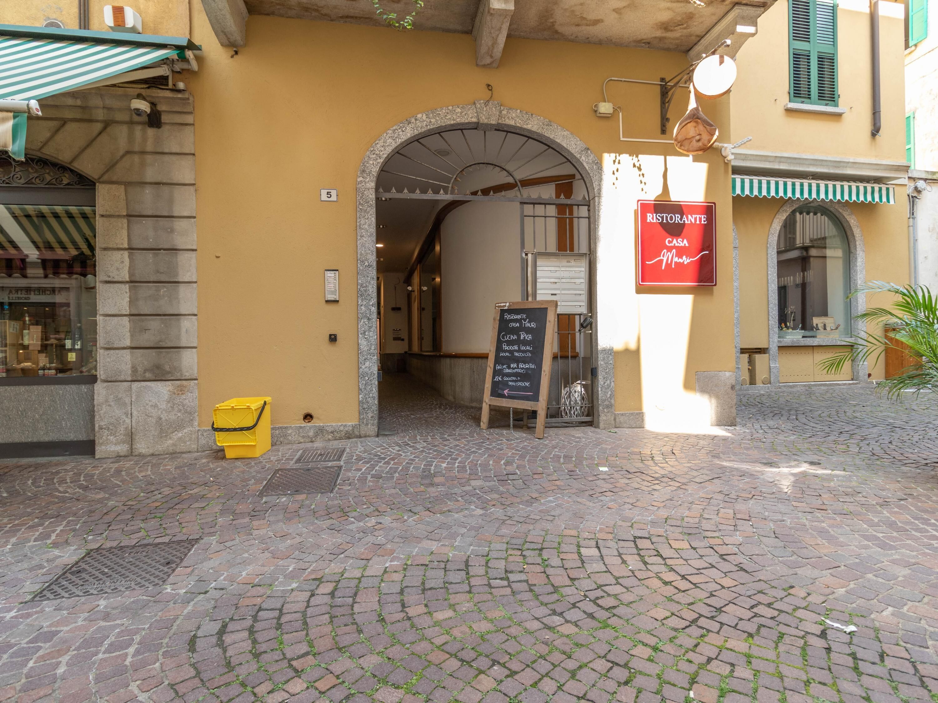 L’entrée d’un restaurant, avec une enseigne indiquant les plats proposés, une poubelle jaune et un trottoir pavé.