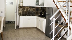 A modern kitchen with white cabinets, a stainless steel refrigerator, and a wooden staircase leading to an upper level. - Casa Delle Mancarelle (Syracuse)