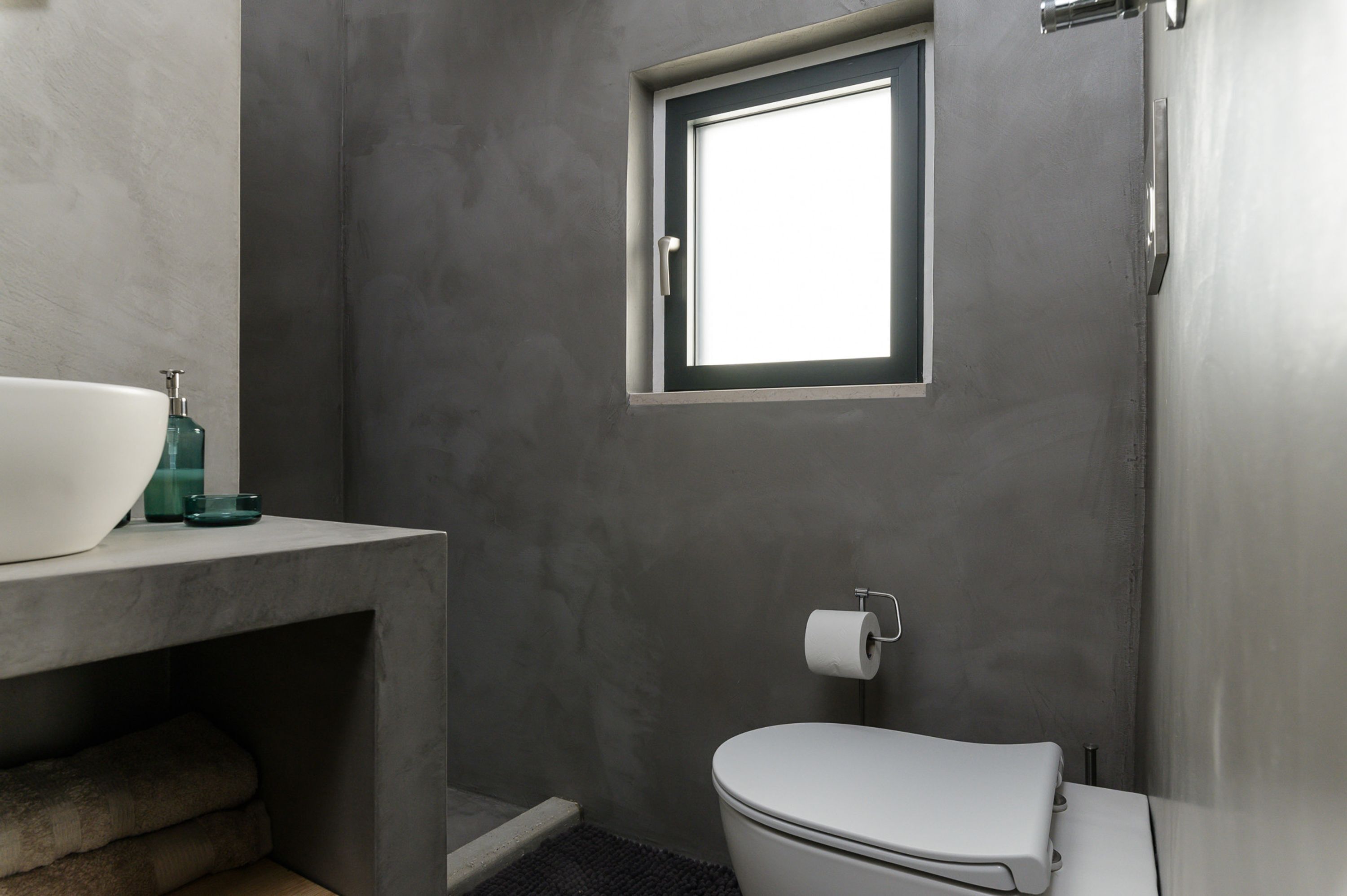 A bathroom with a toilet, a window, and a sink with a soap dispenser.