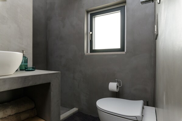 A bathroom with a toilet, a window, and a sink with a soap dispenser.