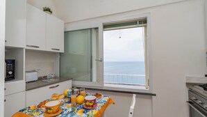 A kitchen with a table set for breakfast, a view of the sea, and a small radio. - L'Aurora house with sea view, WIFI, air conditioning, on the path of the Lemons (Minori)