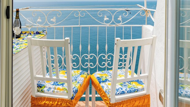 A balcony with two white chairs, a table with a colorful tablecloth, and a view of the sea. - L'Aurora house with sea view, WIFI, air conditioning, on the path of the Lemons (Minori)