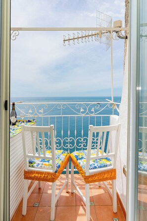A balcony with two white chairs, a table with a colorful tablecloth, and a view of the sea. - L'Aurora house with sea view, WIFI, air conditioning, on the path of the Lemons (Minori)