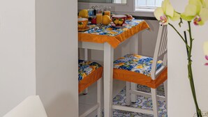 A narrow room with a window overlooking the sea, a table with breakfast items, a bed with a colorful bedspread, and a white chair. - L'Aurora house with sea view, WIFI, air conditioning, on the path of the Lemons (Minori)